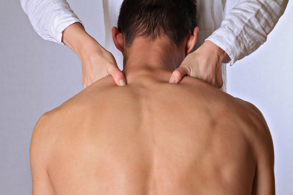 Homme avec le torse nu couché sur le ventre avec les pouces de son chiropraticien sur les épaules, dans le cadre d'un traitement.