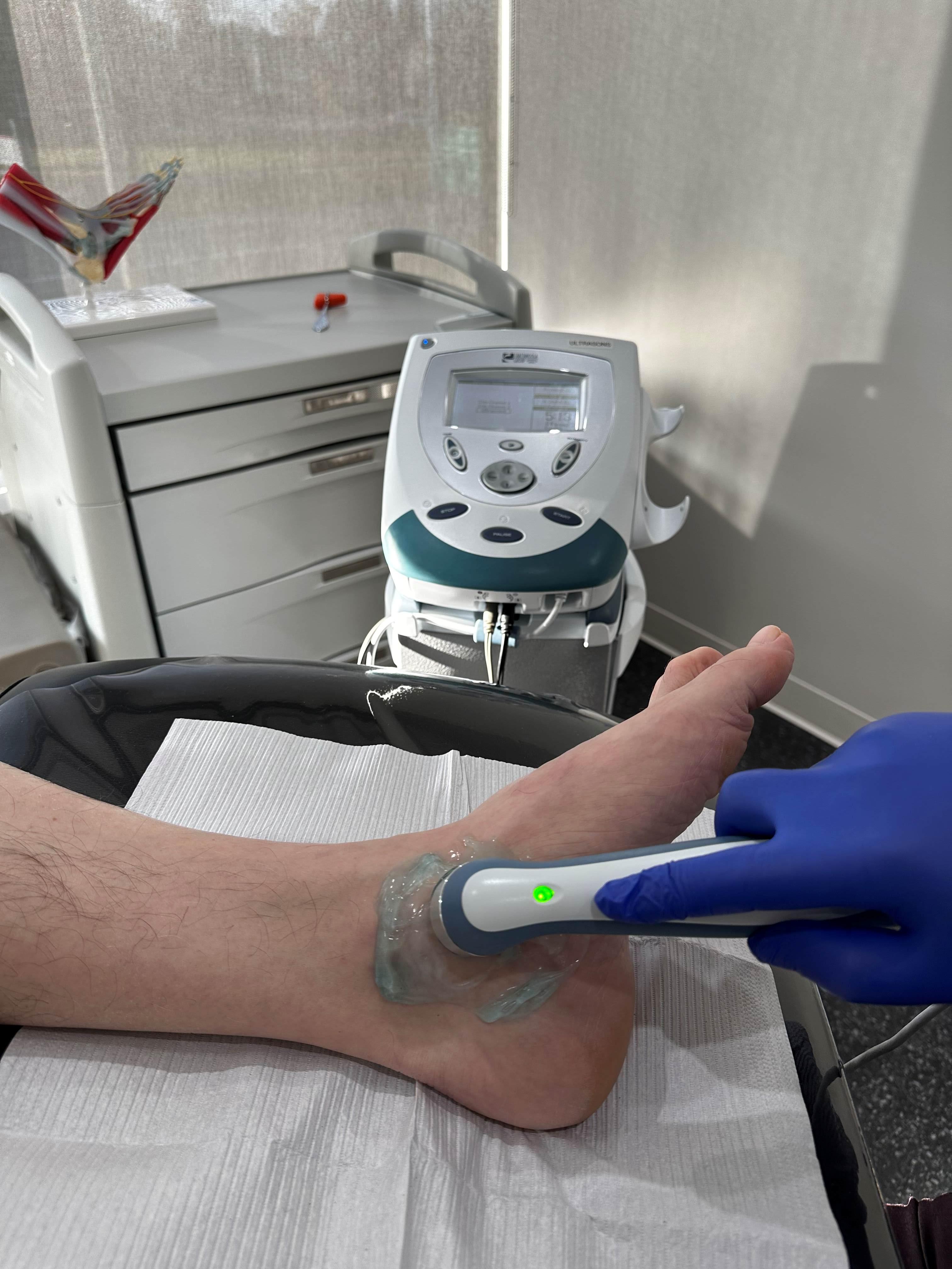 Application d'ultrason avec du gel sur la cheville d'un patient qui est allongé dans le cadre d'un traitement dans une clinique médicale