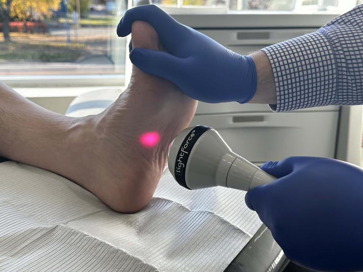 Application de laser dans l'arche du pied d'un patient par un docteur dans le cadre d'un traitement dans une clinique.