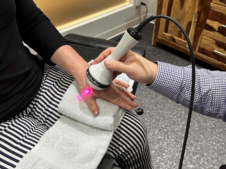 Application de laser sur le pouce d'un patient par un docteur dans le cadre d'un traitement dans une clinique.